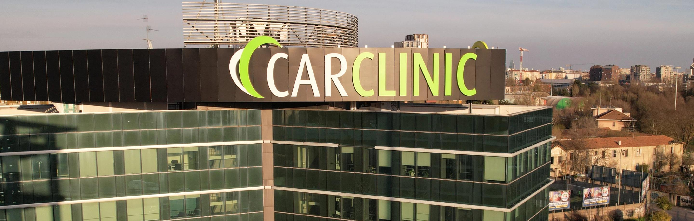 Insegna "CARCLINIC" su edificio con vetro e paesaggio urbano sullo sfondo.
